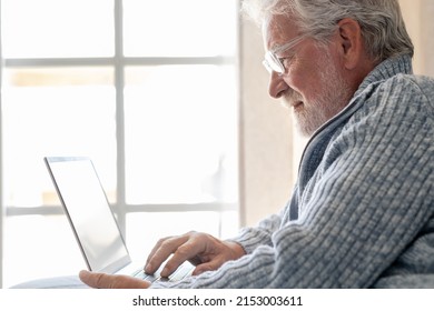 Elderly 70s Man Seated On Sofa Browsing On Laptop, Senior Looking At Laptop Screen Surfing The Net, Older Generation And Modern Tech Application Easy Usage Concept