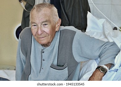 Elderly 90 Years Old Senior Man Dressed In Pajamas Sitting On A Hospital Bed Recuperating From Illness. Elderly Disease, Medical Care, Age Friendly Health System And Hospital Concept.