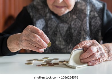 Elderly 95 years old woman sitting miserably at the table at home and counting remaining coins from the pension in her wallet after paying the bills. - Shutterstock ID 1086254576