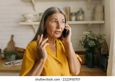 Elderly adorable Caucasian grandmother talking on phone with her grandson standing at kitchen having anxious and worried face expression, looking through window, waiting him for lunch - Shutterstock ID 2122950707