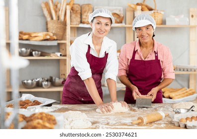 Elderly and adult female bakers kneading dough and cutting dough with scraper - Powered by Shutterstock