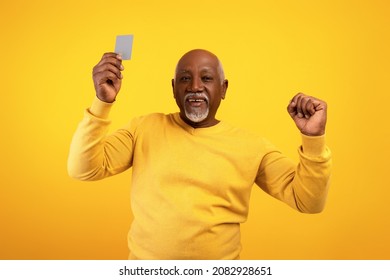 Elderly African American Man Showing Credit Card And Making YES Gesture On Orange Studio Background. Happy Senior Black Male Using Electronic Money, Celebrating Big Win Or Success