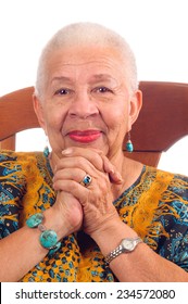 Elderly African American Woman Sitting In A Chair Clasping Hands And Smiling