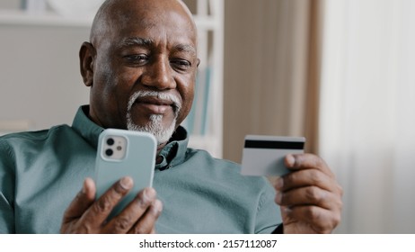 Elderly African Dominican old mature man at home online transaction buying hold smartphone credit card successful payment buy on internet with mobile app food delivery order with phone easy e-payment - Powered by Shutterstock