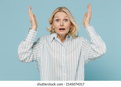 Elderly angry shocked indignant caucasian woman 50s wear striped shirt spread hands look camera scream isolated on plain pastel light blue color background studio portrait. People lifestyle concept
