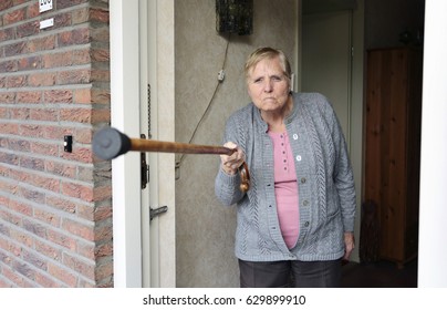 Elderly angry woman threatening with a cane in the doorway