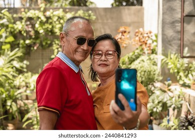 An elderly asian couple enjoys the outdoors by taking a selfie to capture a moment of their shared happiness. - Powered by Shutterstock