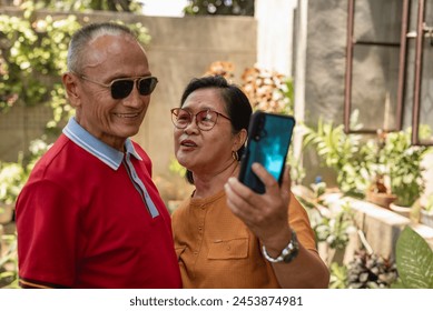 An elderly asian couple enjoys the outdoors by taking a selfie to capture a moment of their shared happiness. - Powered by Shutterstock