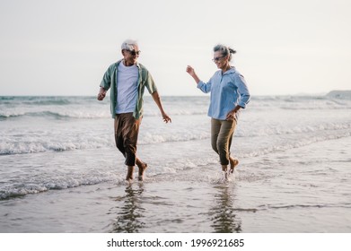 Elderly Asian couple having fun on the beach at sunset - Powered by Shutterstock