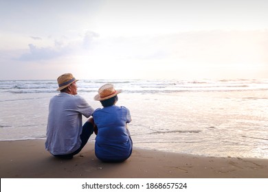 An elderly Asian couple sitting on the beach Look at the beautiful sea in the morning together. Travel concept to live happily in retirement age. copy space