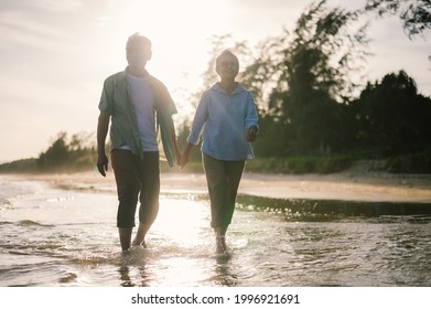 Elderly Asian Couple Walking On The Beach At Sunset