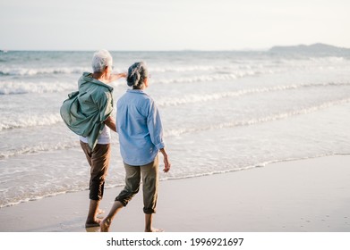 Elderly Asian Couple Walking On The Beach At Sunset