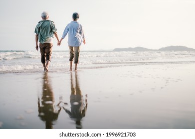 Elderly Asian Couple Walking On The Beach At Sunset