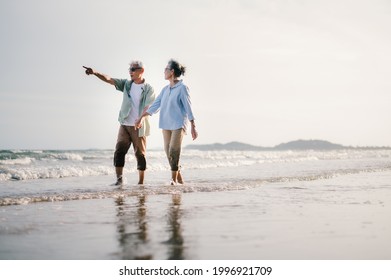 Elderly Asian Couple Walking On The Beach At Sunset