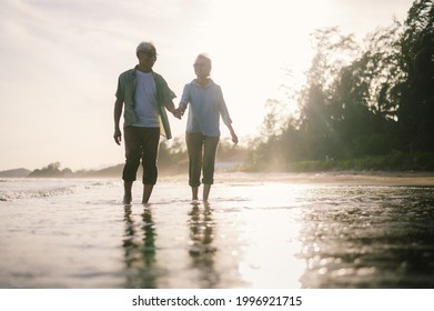 Elderly Asian Couple Walking On The Beach At Sunset