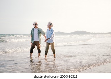 Elderly Asian Couple Walking On The Beach At Sunset