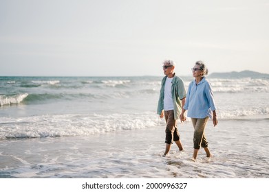 Elderly Asian Couple Walking On The Beach At Sunset