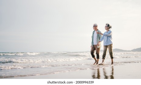 Elderly Asian couple walking on the beach at sunset - Powered by Shutterstock