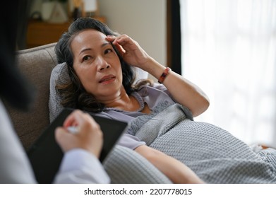 An Elderly Asian Female Patient Talking With Her Doctor In The Recovery Room. Medical Checkup Concept. Close-up Image