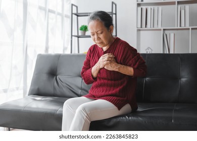 Elderly asian housewife woman sitting on sofa. Heart disease, chest pain, irregular heartbeat - Shutterstock ID 2263845823