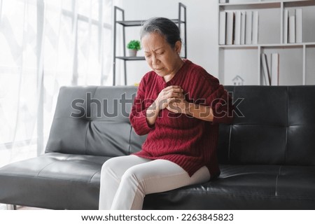 Elderly asian housewife woman sitting on sofa. Heart disease, chest pain, irregular heartbeat