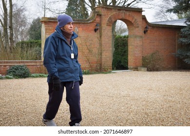 Elderly Asian Indian Woman Exercising, Walking Outdoors In Winter, UK. Wearing Warm Clothing And An SOS Personal Safety Alarm Pendant