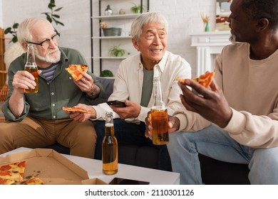 Elderly Asian Man Holding Remote Controller And Talking To Multiethnic Friends With Beer And Pizza At Home