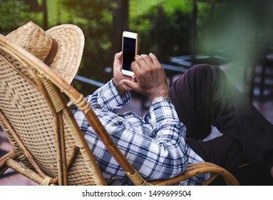An elderly Asian man sitting using a mobile phone. 