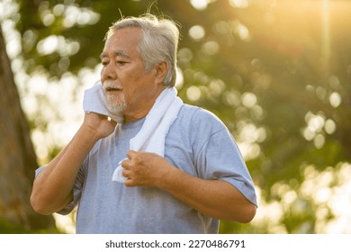 Elderly Asian man in sportswear wiping sweat on his face with towel during jogging exercise at park at summer sunset. Healthy retired person enjoy outdoor lifestyle sport training running workout. - Powered by Shutterstock