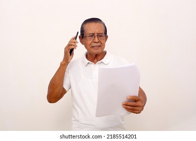 Elderly Asian Man Standing While Talking On The Phone And Holding Papers. Isolated On White