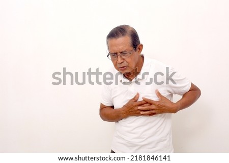 Elderly asian man standing while holds his chest, suffering from chest pain. Isolated on white