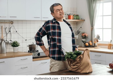 elderly Asian man strains his back carrying a heavy shopping bag with healthy food ingredients from the market or store, mindful of his health. - Shutterstock ID 2337561679