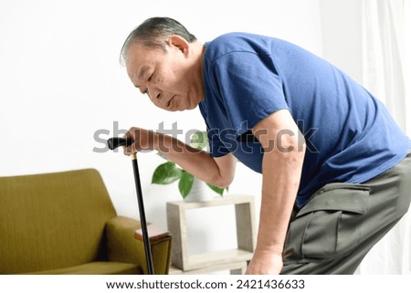 An elderly Asian man suffering while using a cane