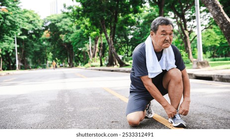 Elderly Asian man tying shoelaces on a park path, preparing for exercise. The Asian man is focused on fitness in the park. Healthy elderly Asian man tying running shoes in the park.  - Powered by Shutterstock