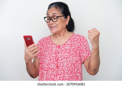 Elderly Asian woman clenched fist while looking to her mobile phone