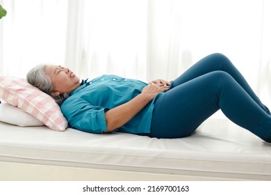 An elderly Asian woman lies in bed with acute abdominal pain at home. Concept of problems of gastrointestinal tract in the elderly. Indigestion. Cholecystitis. health care