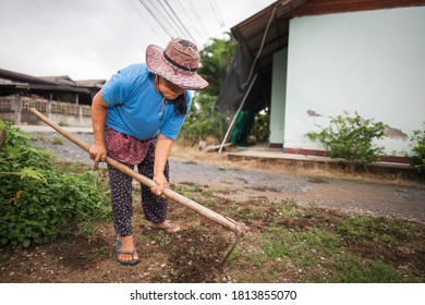 An Elderly Asian Woman Purges The Grass Around The House.