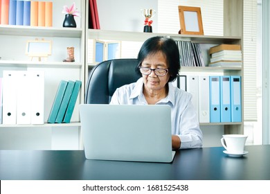 An Elderly Asian Woman Sitting At Work Typing A Notebook Computer In An Office. The Concept Of Senior Employment, Social Security