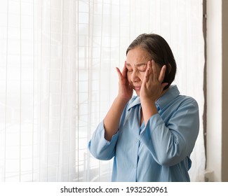 Elderly Asian woman standing and having a headache and touching her head with her hands at home. Asian older lonely woman. Retirement, quarantine and health care concept - Powered by Shutterstock