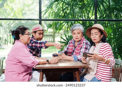 Elderly Asian women gathered around a wooden table in a bright cafe, engaging in a friendly discussion. One woman pointing while others listen attentively. Casual clothing, natural light, - Powered by Shutterstock