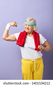 Elderly attractive woman with a happy, proud and satisfied expression on face, raising one hand, showing strength of her musculs, celebrating sport achievement.