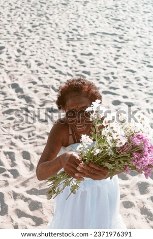 Elderly Black woman celebrating at the beach with flowers, Yemanja festival, tossing flowers on the beach. Brazil traditional celebration. Elderly black woman with flowers