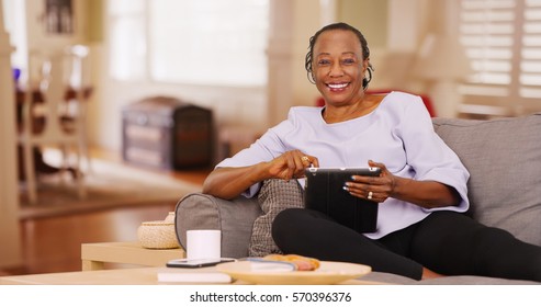 An Elderly Black Woman Happily Uses Her Tablet While Looking At The Camera