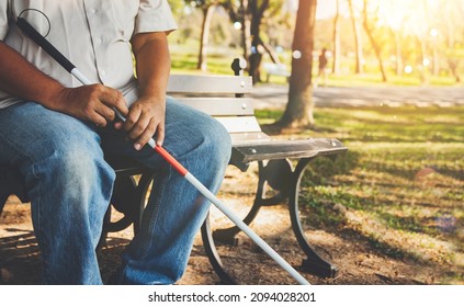 Elderly blind man with a blind cane sits alone on a park bench : Lind man who wants peace and lives in solitude concept.