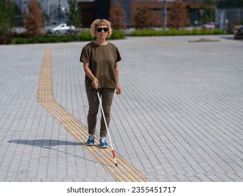 An elderly blind woman walks with a cane along a tactile tile.  - Powered by Shutterstock