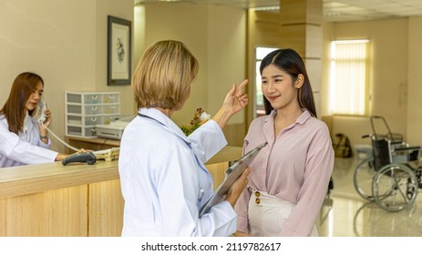 Elderly Blonde Hair Surgical Doctor Discusses With Her Patient For A Cosmetic Or Beauty Treatment Program At Reception Desk. Female Girl Gets Suggestion From A Female Doctor In A Beauty Clinic