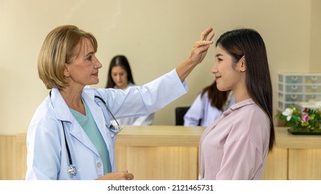 Elderly Blonde Hair Surgical Doctor Discusses With Her Patient For A Cosmetic Or Beauty Treatment Program At Reception Desk. Female Girl Gets Suggestion From A Female Doctor In A Beauty Clinic