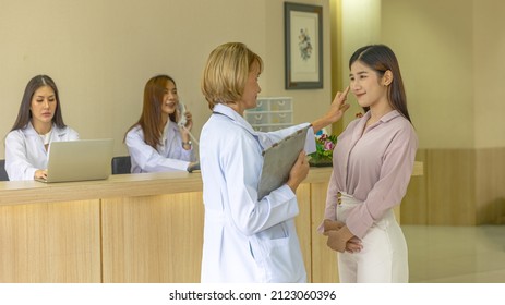 Elderly Blonde Hair Surgical Doctor Discusses With Her Patient For A Cosmetic Or Beauty Treatment Program At Reception Desk. Female Girl Gets Suggestion From A Female Doctor In A Beauty Clinic