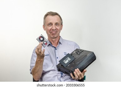 Un hombre anciano, de ojos azules y satisfecho inserta una cinta en una antigua grabadora de cinta de tambor a cinta para escuchar una grabación de audio en un fondo claro