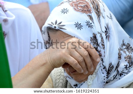 Elderly Bosnian woman weeps in graveyard in Memorial centre Srebrenica. Mass funeral of war victims in Potočari. Burial ceremony  of genocide victims in 1995. Muslim woman cries at grave. Srebrenica